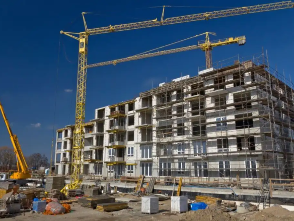 A high-rise condominium building actively under construction with visible scaffolding, concrete pillars, and tower cranes, illustrating a pre-selling property development.