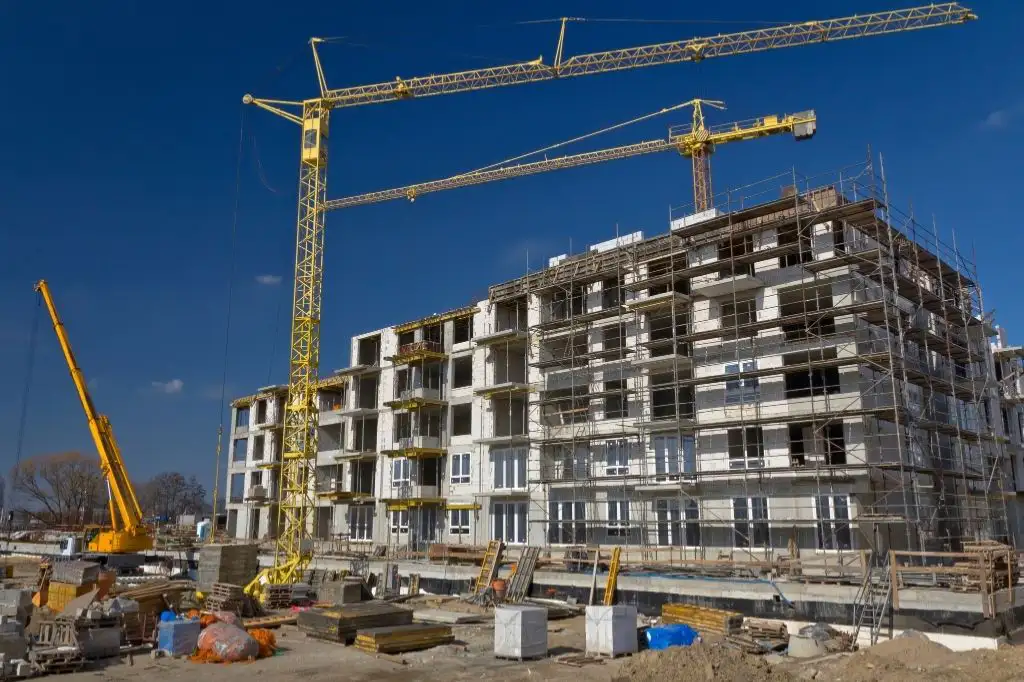 A high-rise condominium building actively under construction with visible scaffolding, concrete pillars, and tower cranes, illustrating a pre-selling property development.